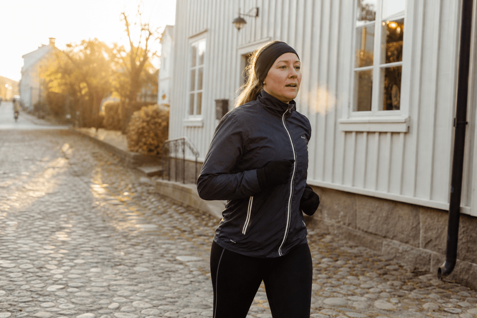 Kvinna på en rask löprunda på en kullerstensgata i en svensk småstad i tidigt morgonljus.